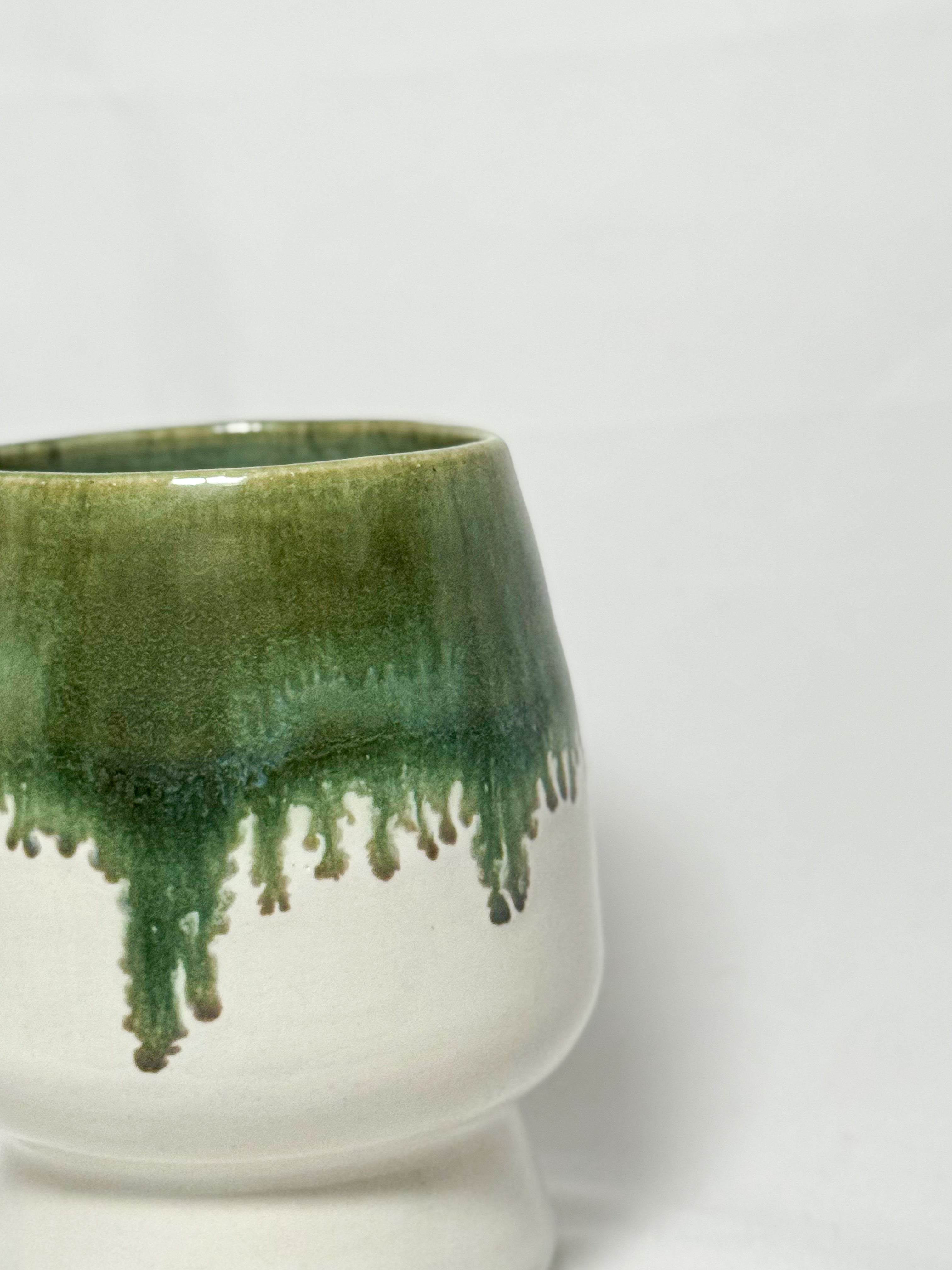 closeup view of the rim of a ceramic stoneware vase with mossy green glaze dripping down into a white glaze