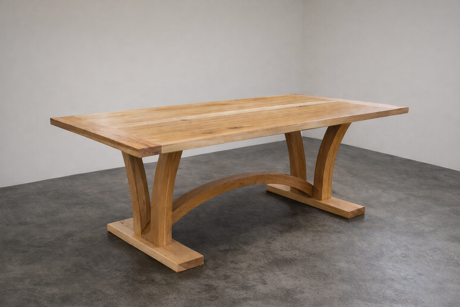 A custom hickory dining table with curved trestle legs in a room with white walls and a concrete floor 