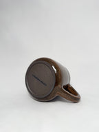 The bottom of a brown marbled stoneware mug that shows a smooth hand trimmed foot and 'elmstone studio' branding 
