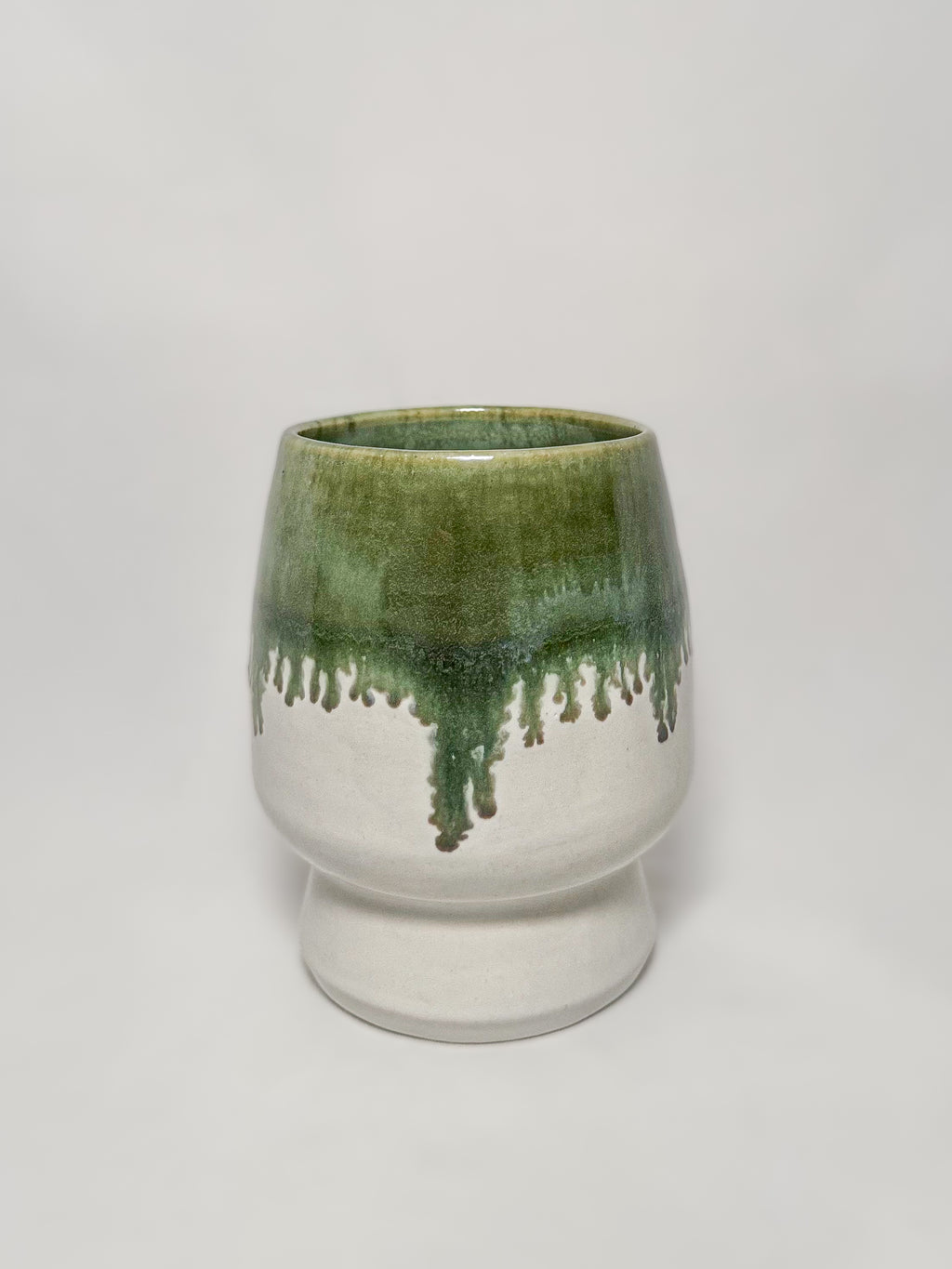A ceramic stoneware vase with mossy green glaze dripping down into a white glaze