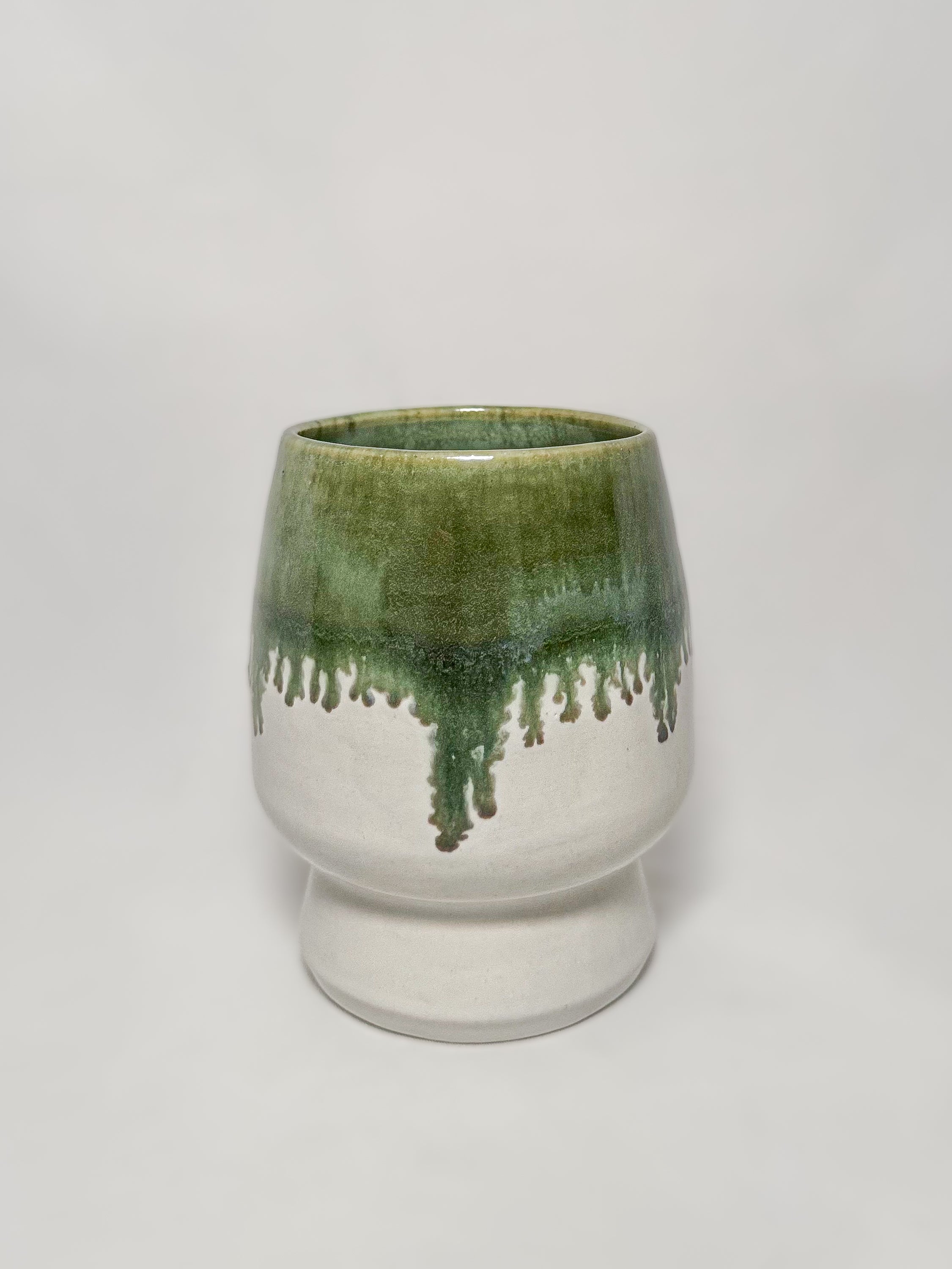 A ceramic stoneware vase with mossy green glaze dripping down into a white glaze