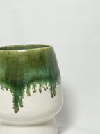 closeup view of the rim of a ceramic stoneware vase with mossy green glaze dripping down into a white glaze