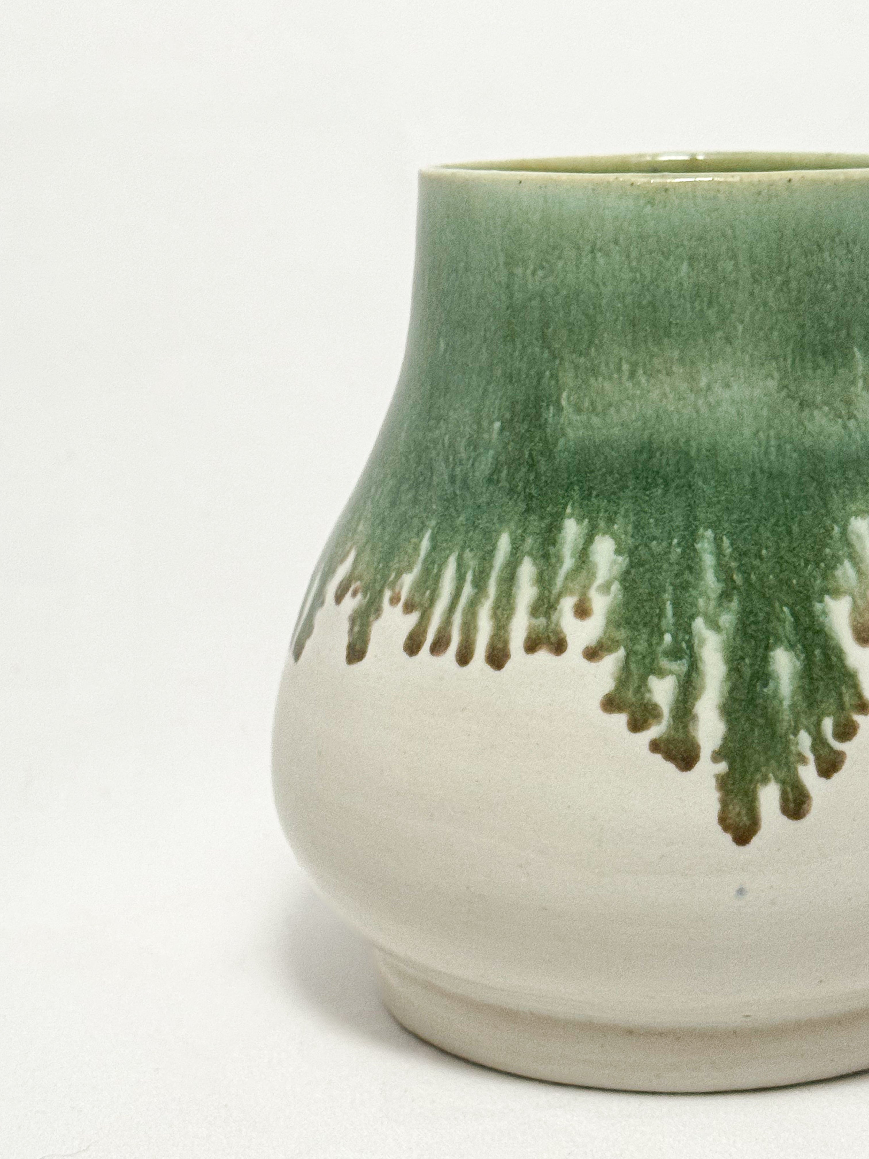 A ceramic stoneware vase with mossy green glaze dripping down into a white glaze