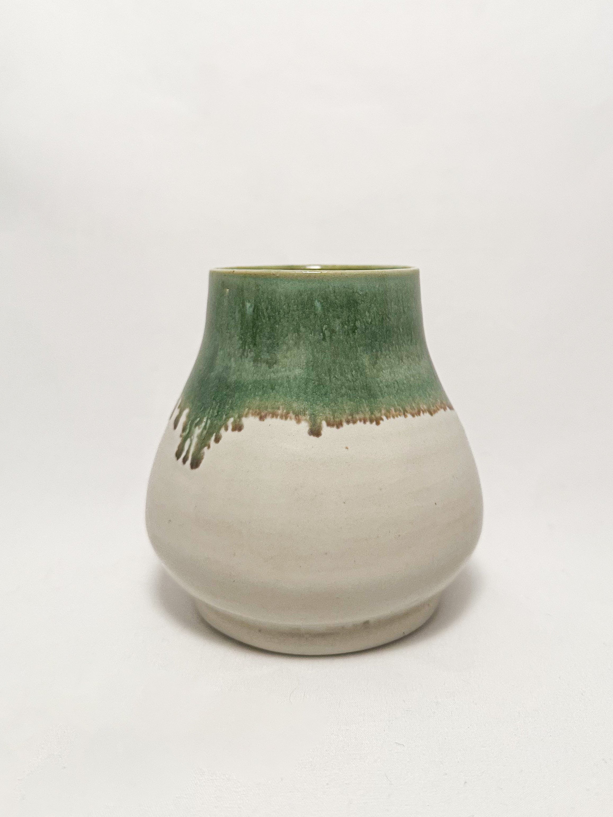 A ceramic stoneware vase with mossy green glaze dripping down into a white glaze
